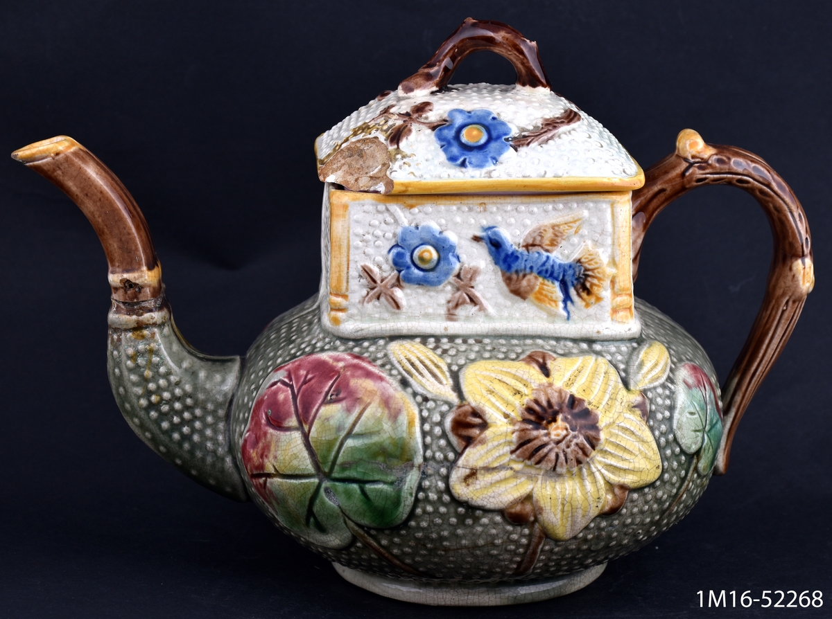 Tekanna, nedre delen tryckt klotformig, övre delen 4-kantig, dekor fågel, blommor och blad i relief, många kulörer och guld.