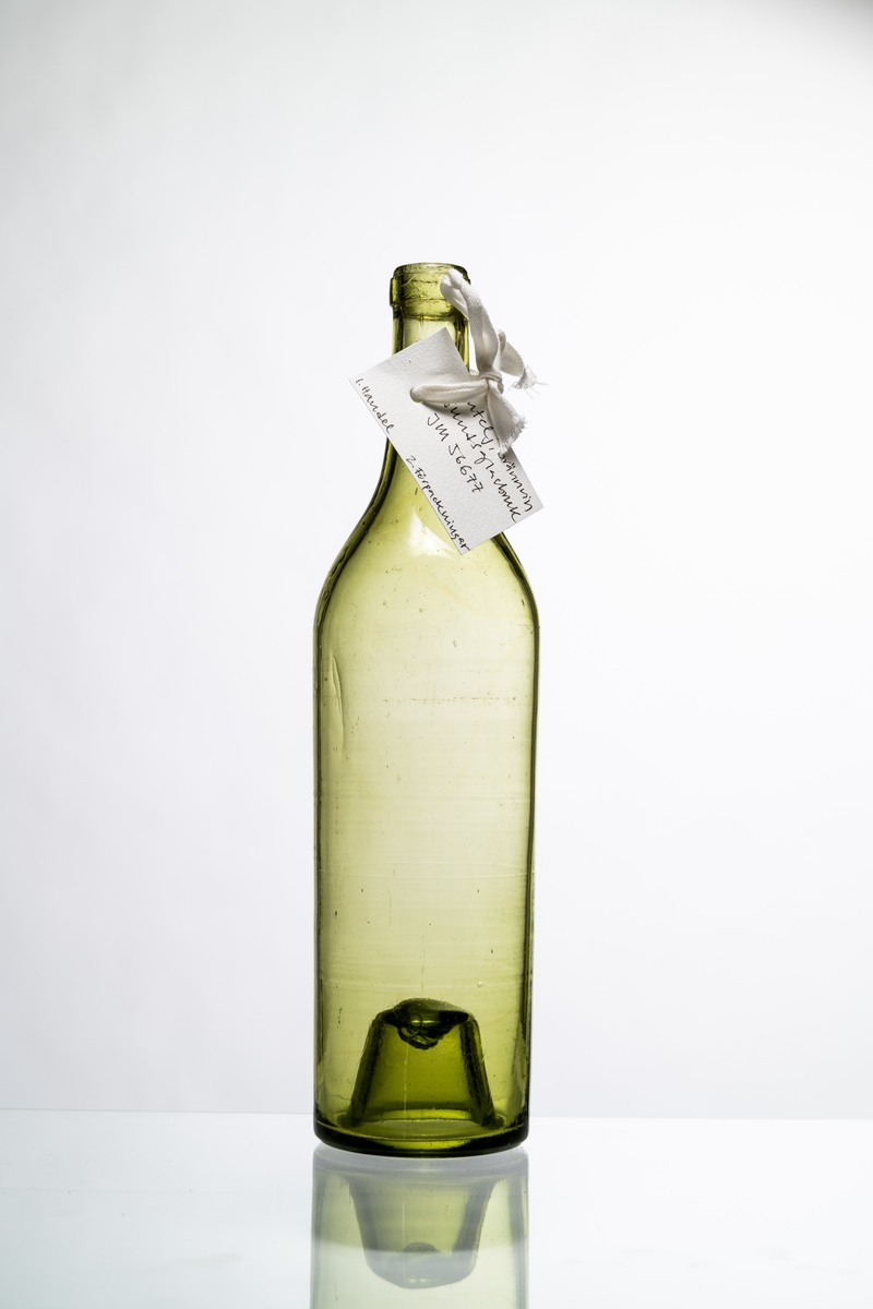 Butelj för brännvin av ljust grönt glas, avsedd för tillslutning med naturkork. Buteljen har "Kinnekullebotten" med liten kula. Blåsor i glaset. Hantverksmässigt tillverkad vid Sunds glasbruk, Jönköpings län. Se vidare Historik.