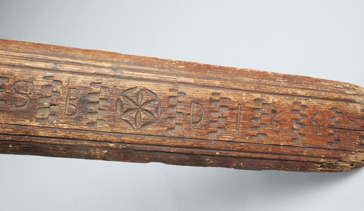 Mangelbräde i brunbetsad ek. Handtaget infällt, spikat med träplugg, (skadat, träbortfall). Bruks- och färgslitage. Lätt maskstungen fram. Översidan med dekor av bladrosett, nagelsnitt, initialer m.m., samt skuret "SBD 1667". Dubbelprofilerade rundade långsidor. (Gunnar Blomgren)

Mangelbräde eller kavelbräde är ett redskap av trä som använts för mangling av textilier. Mangelbrädet användes tillsammans med en kavel, en slät rulle av trä. Den textil som skulle manglas, rullades upp på kaveln, på ett bord eller annat slätt underlag. Under hårt tryck, rullades kaveln med hjälp av mangelbrädet, fram och tillbaka över bordet. (Wikipedia)