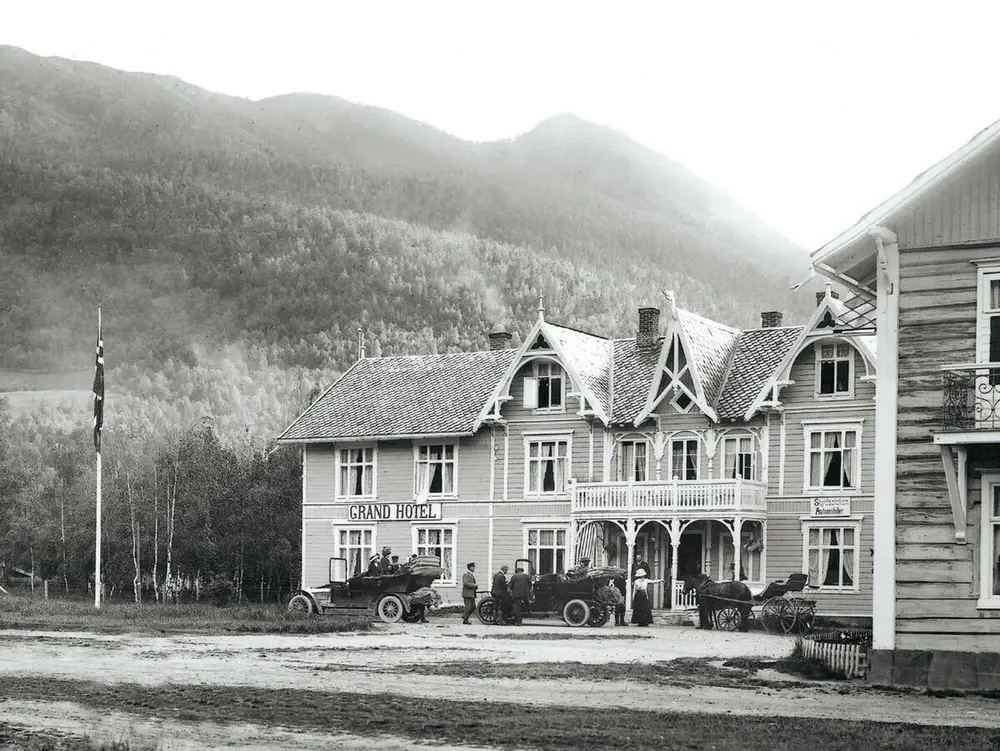 Fotografi av Grand hotel Otta, tidlig 1900-tall med tre biler ute på plassen foran hotellet.