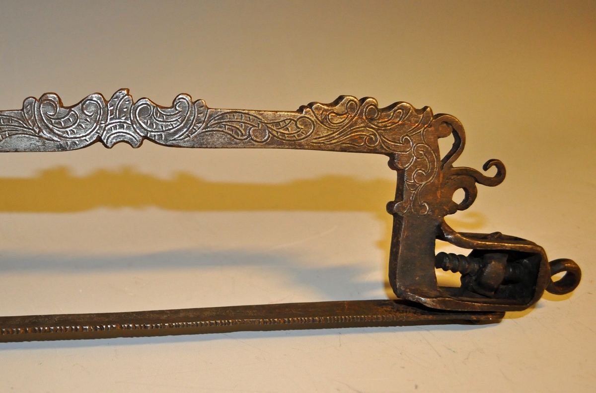 Fra protokollen: Haandsag af jern, særlig for tilvirkning af nøgler. Dreiet haandtak. Fin rokokkogravering og merket I. P. S. 1798. Dreiet haandtak.