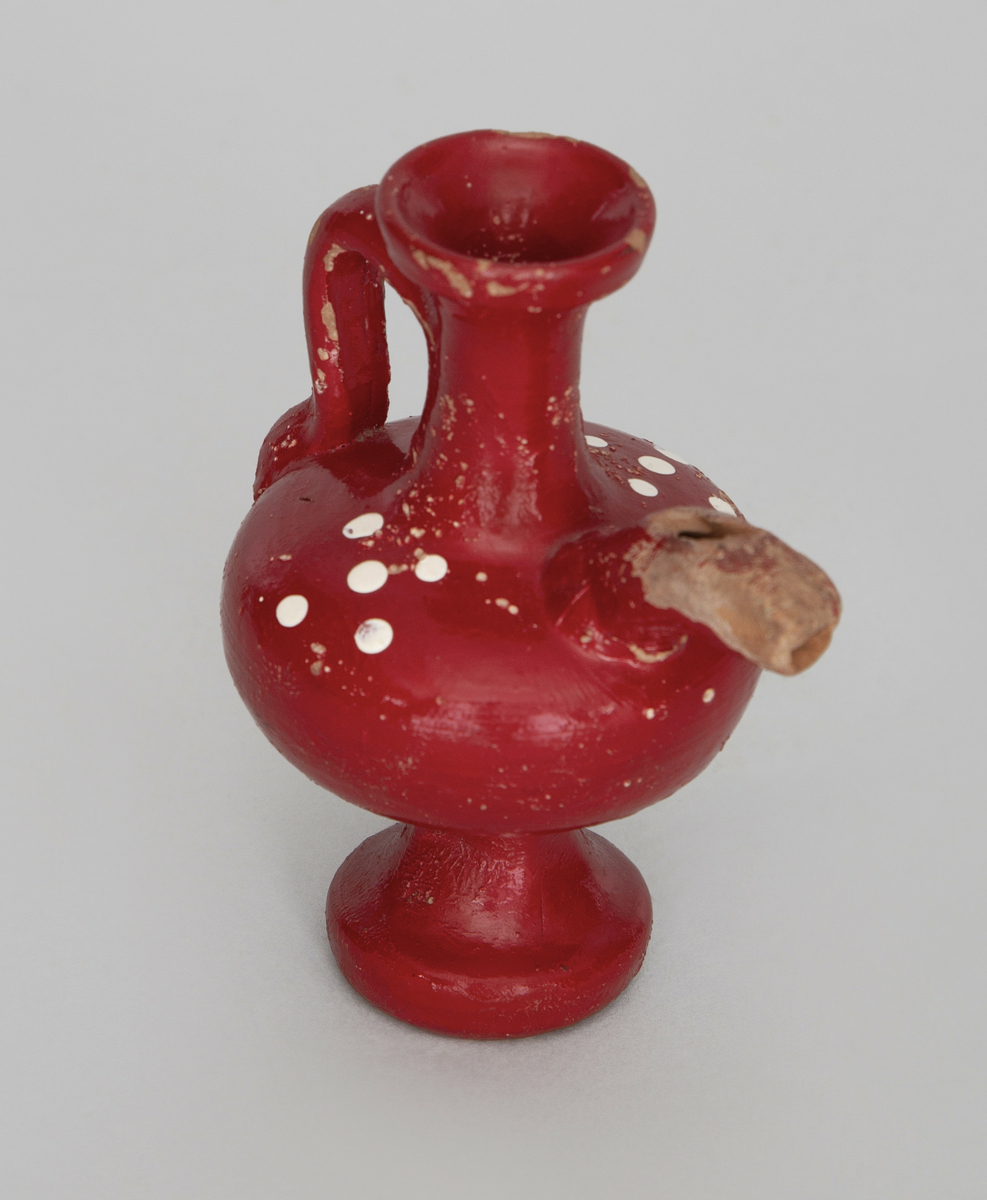Spaltefløyte. Vannfløyte av keramikk formet som en liten vase med stett, klokke og hals, tut og hank.
Halsen er åpen øverst for påfylling av vann. Spalte og labium i tuten.
Utvendig dekorert med rød glasur med hvit prikkdekor.


