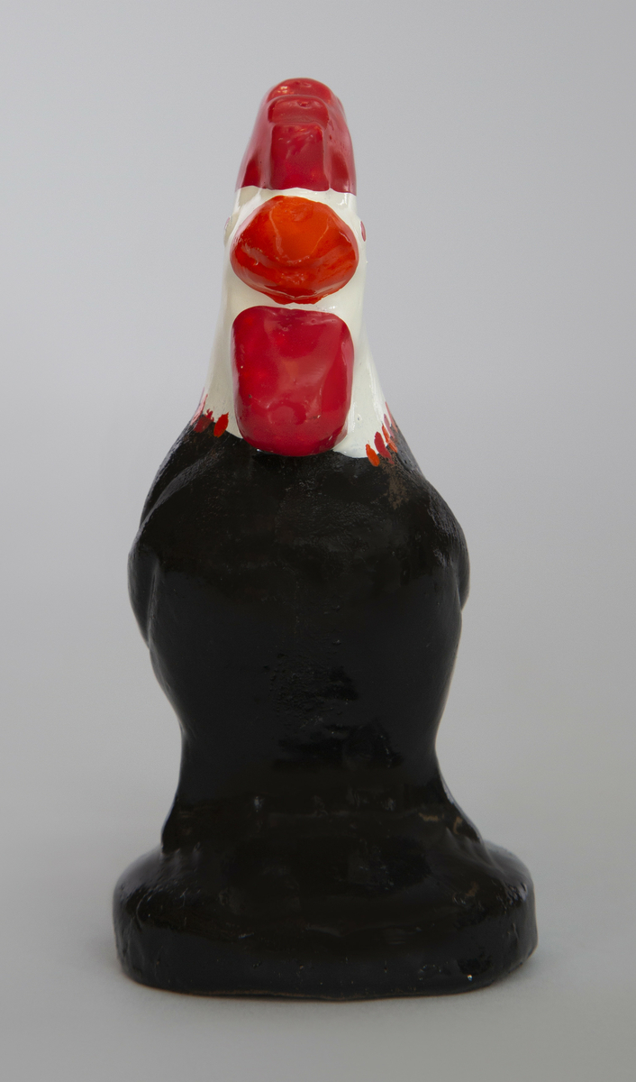 Spaltefløyte i keramikk i form av en hane på en rund sokkel. Utvendig glasert: kam, pose og nebb rød, hode hvitt, korpus og sokkel svart.
Spalte og labium i stjerten.
Ett fingerhull.

