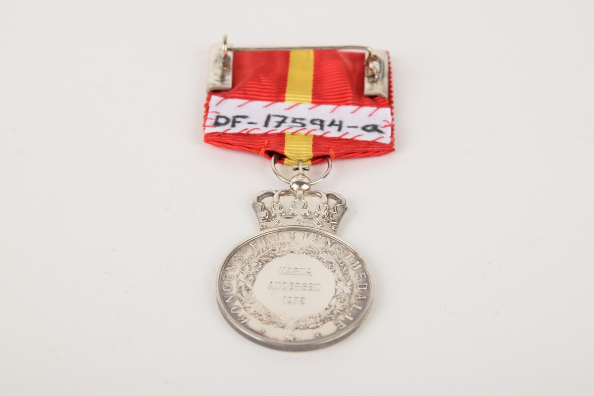 Et eksemplar av "Kongens fortjenstmedalje" i originalt etui. 

Sirkulær medalje med ordensbånd, oppbevart i rektangulært etui. Etuiet har motiv av en krone i sølv på lokket.
