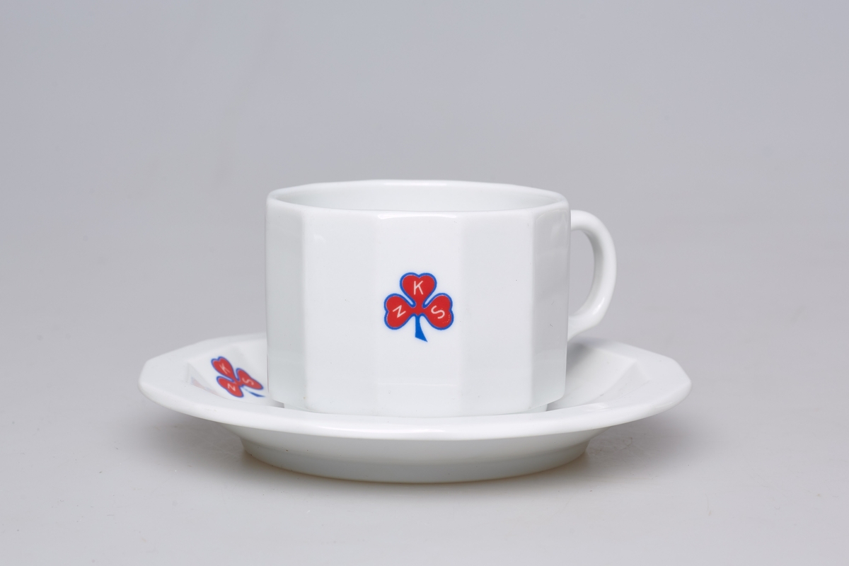 Kaffekopp med skål i tykt porselen. Både kopp og skål er 12-kantet har logoen til Norske kvinners sanitetsforening. Med tilhørende asjett, TM-16060. 