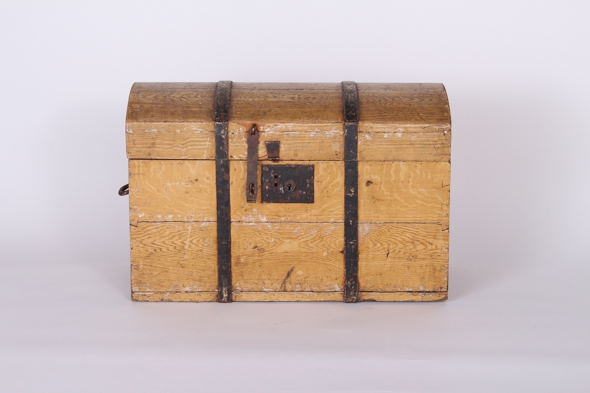 Rektangulær kiste med buet lokk. Jernbeslag på lokk og hjørnene. Håndtak på begge kortsidene. Låsbeslag og lås.
