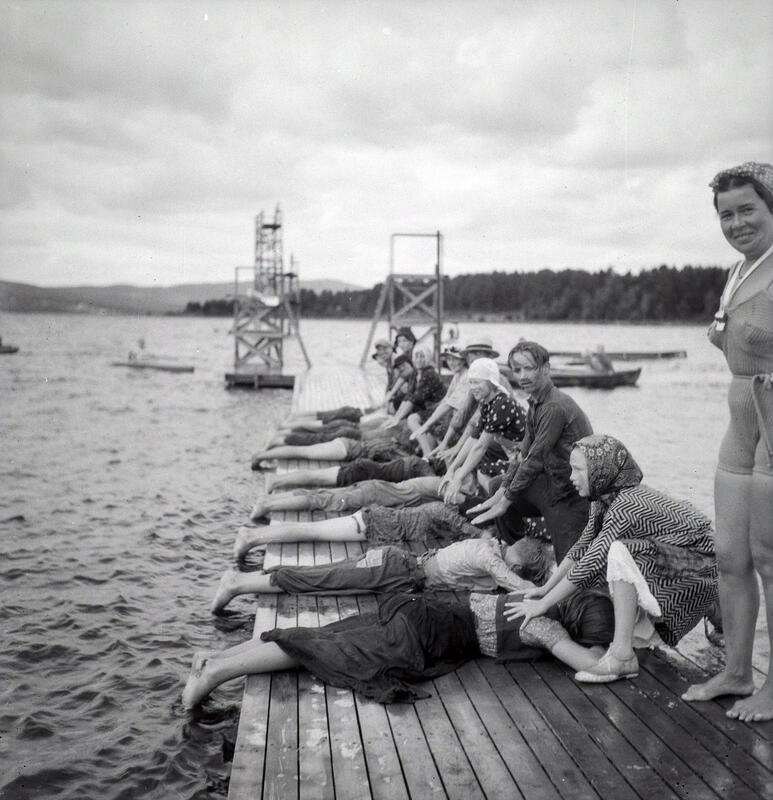 Barn ligger påkledd på magen på en brygge mens de har hver sin medhjelper til å trene på svømmeteknikk. (Foto/Photo)