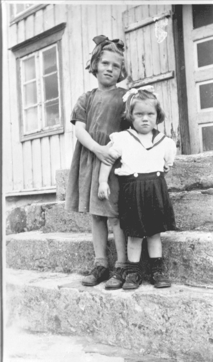 To småjenter stående på steintrapp foran bolighus.