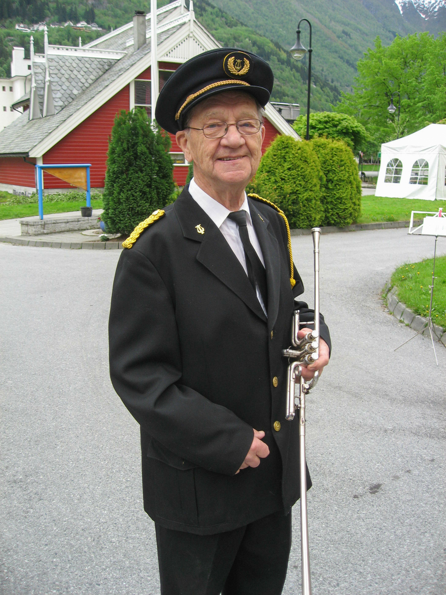 Harald Knutsson med blåseinstrument i Odda musikkorps si uniform framfor ungdomshallen.