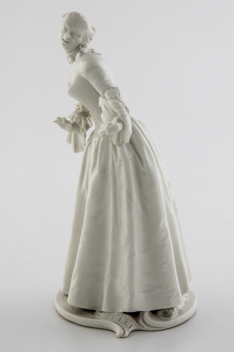 Hvitglasert, umalt porselensfigur av en stående kvinne i 1700-talls klær med uttrykksfull ansiktsmimikk. Kvinnen gjør en avvisende bevegelse mot venstre, med overkroppen lett foroverbøyd. Figuren identifiseres som Isabella, en rolleskikkelse fra comedia dell´arte.