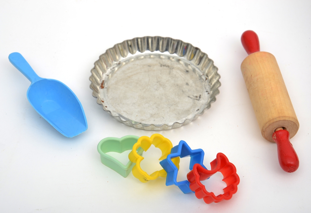 Bakeleketøy bestående av et kjevle i tre, fire ulike plastpepperkakeformer i forskjellige farger, en melskuffe i plast og ei paiform i metall