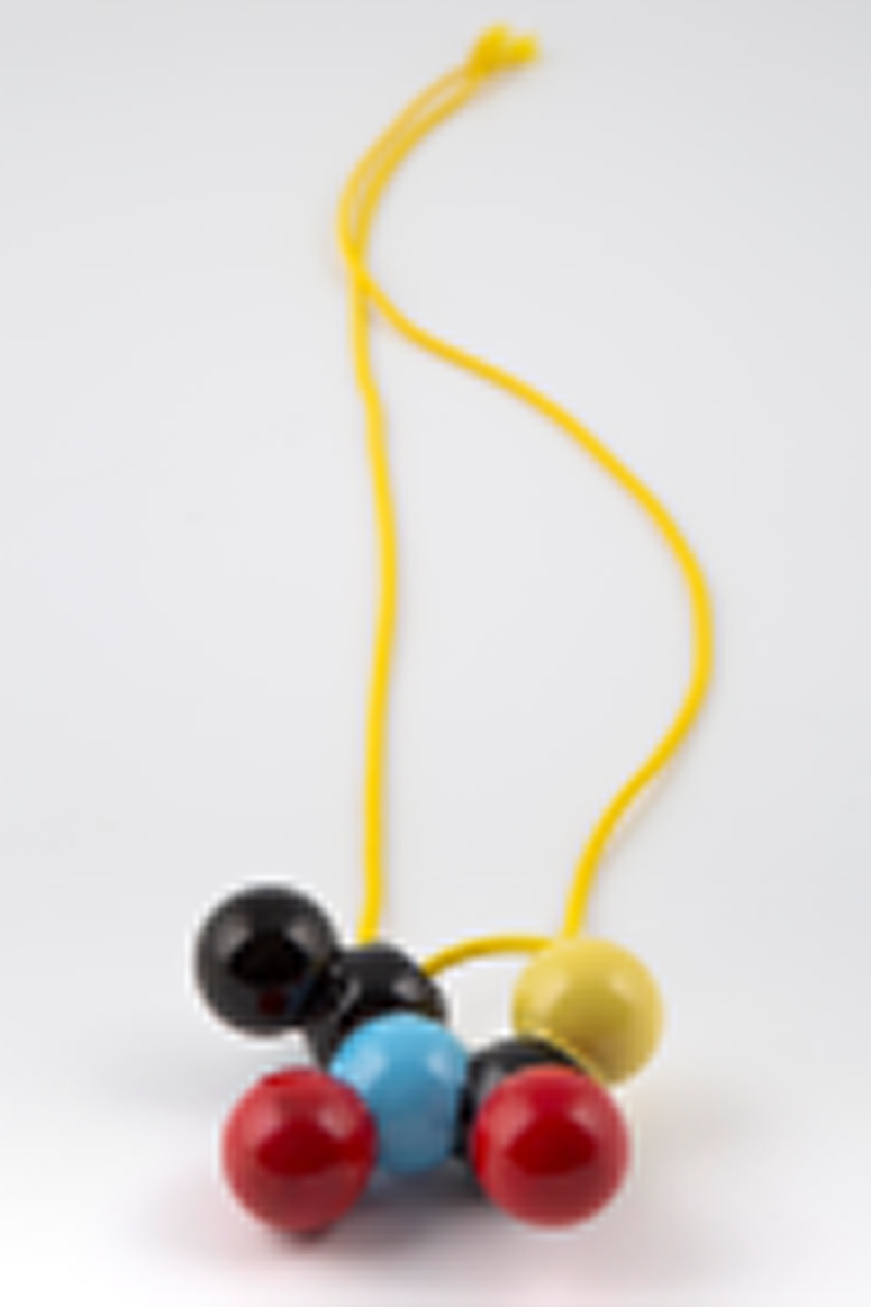 Halssmykke med gult kjede av gummitråd og et anheng i emaljert kobber. Anhenget består av en klynge kuler i primærfargene rødt, blått og gult samt svart.