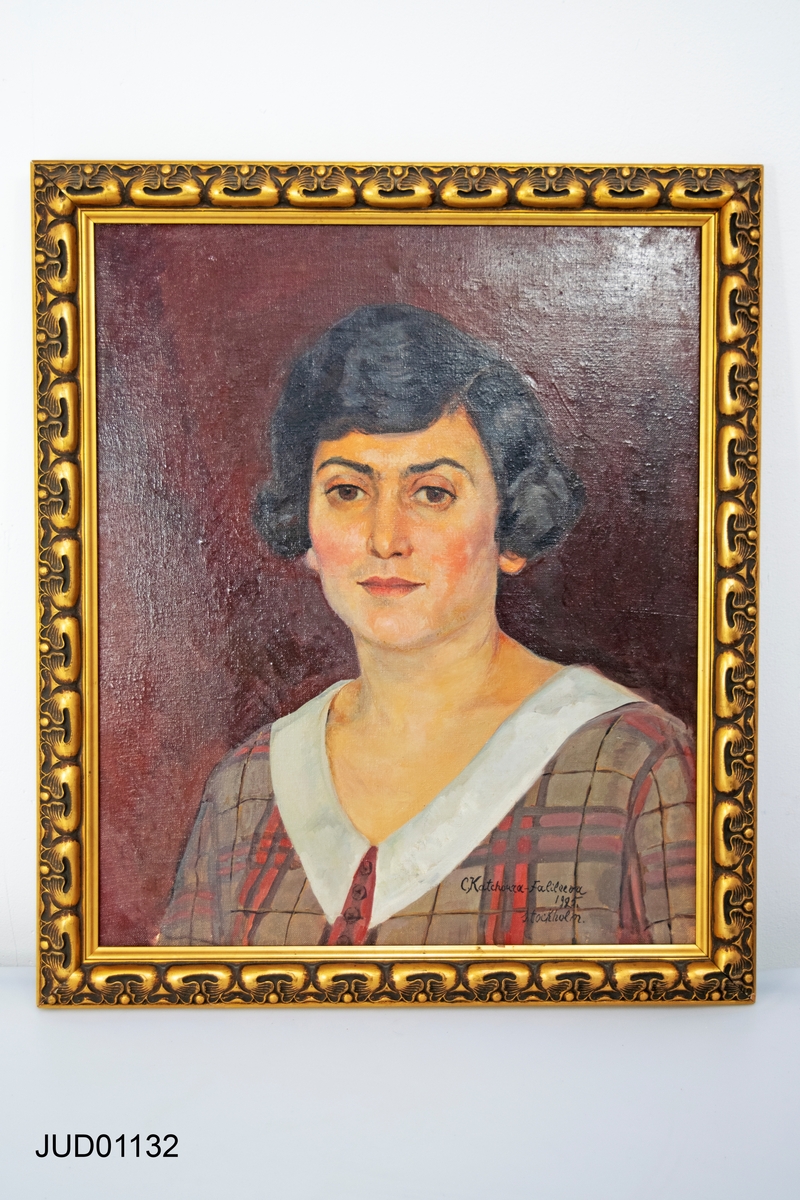 Porträtt av kvinna i rutig blus mot röd bakgrund.