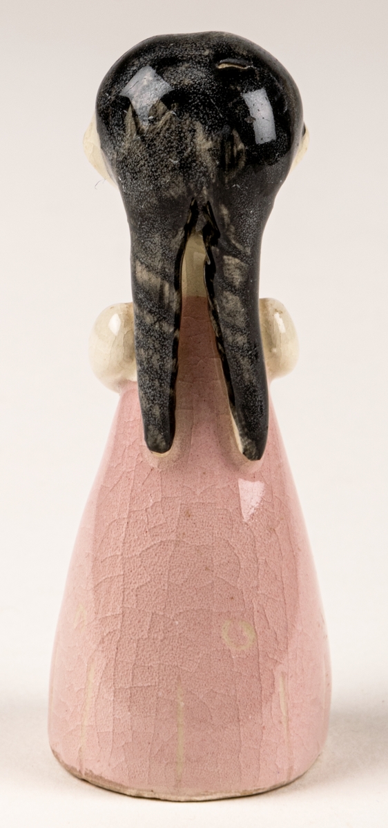 Brudtärna till figuringrupp Brudfölje. Tärnan har mörkt hår och rosa klänning. Formgiven av Dorothy Clough 1955, Gefle Porslinsfabrik. På undersidan svaga rester av stämpeltryckt logga med GEFLE och tre rundugnar.
