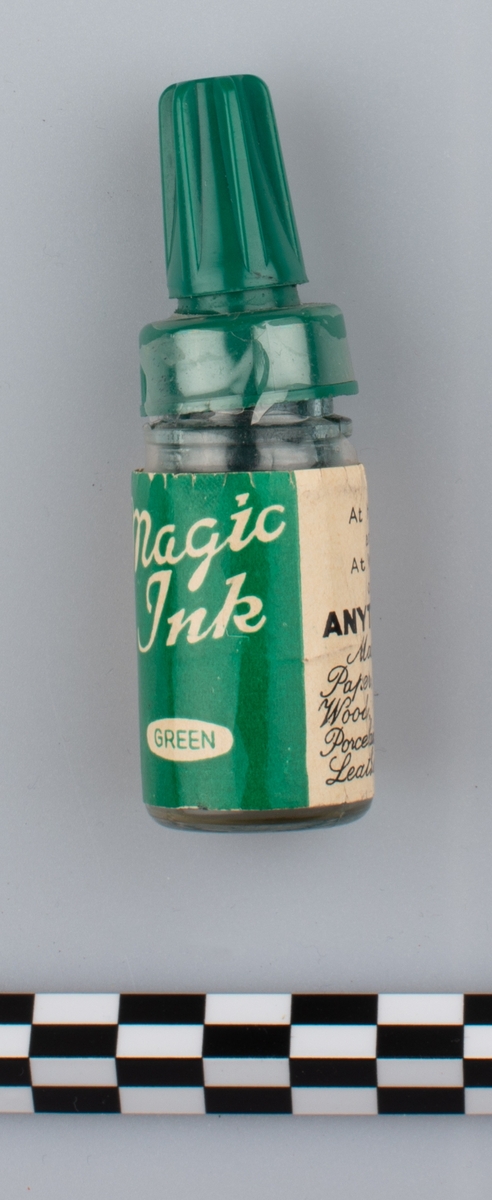 Flaske i klart glass med etikett og grøn tut med grønt lokk