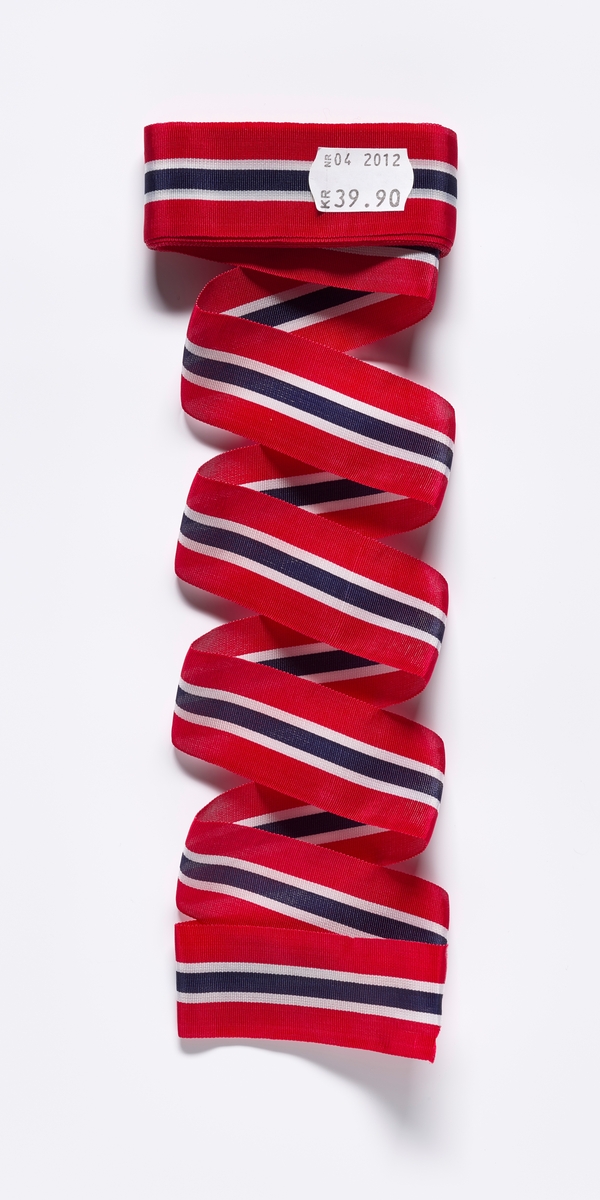 Et sløyfebånd i fargene til det norske flagget, rødt, hvit og blåt. Sløyfebåndet er rullet sammen for salg og det er et prismerke på forsiden med prisen på sløyfebåndet kr. 39,90 - På baksiden er det et klistermerke med fabrikkasjonsmerke  fra Flaggfabrikken A.S Larvik og strekkode.

Sløyfebåndet er samlet inn i forbindelse med prosjektet 17. mai som kulturmøte 2014.