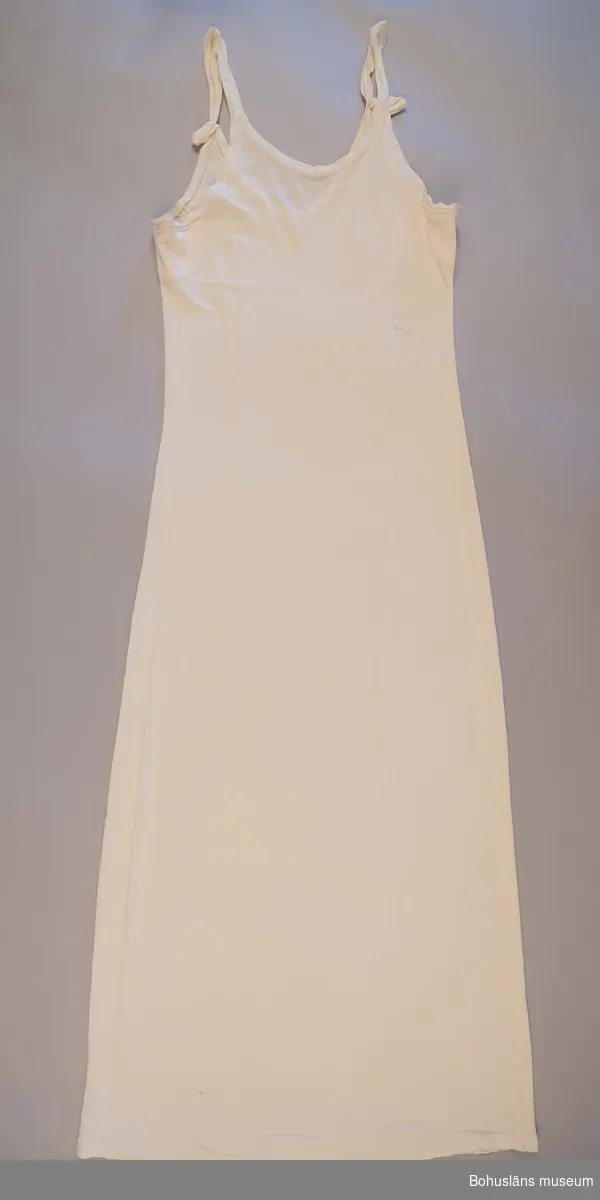 Slät vit underklänning för ung kvinna med axelband i tunn trikå av bomullskvalitet.
Sammanhör med konfirmationsklänning, se UM026650 för uppgifter om denna, konfirmationen samt brukaren.
