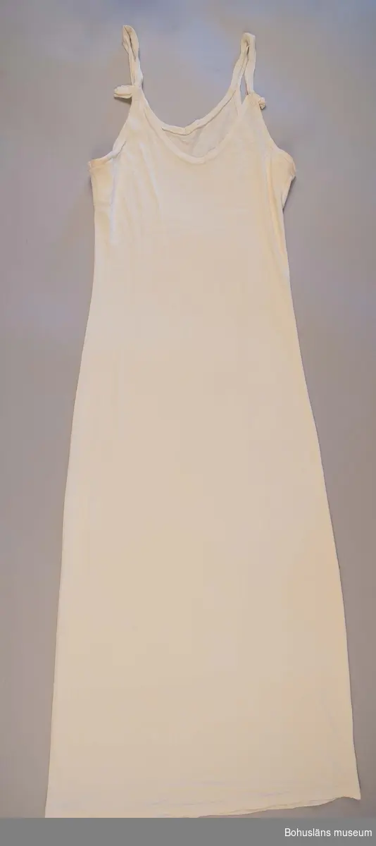 Slät vit underklänning för ung kvinna med axelband i tunn trikå av bomullskvalitet.
Sammanhör med konfirmationsklänning, se UM026650 för uppgifter om denna, konfirmationen samt brukaren.
