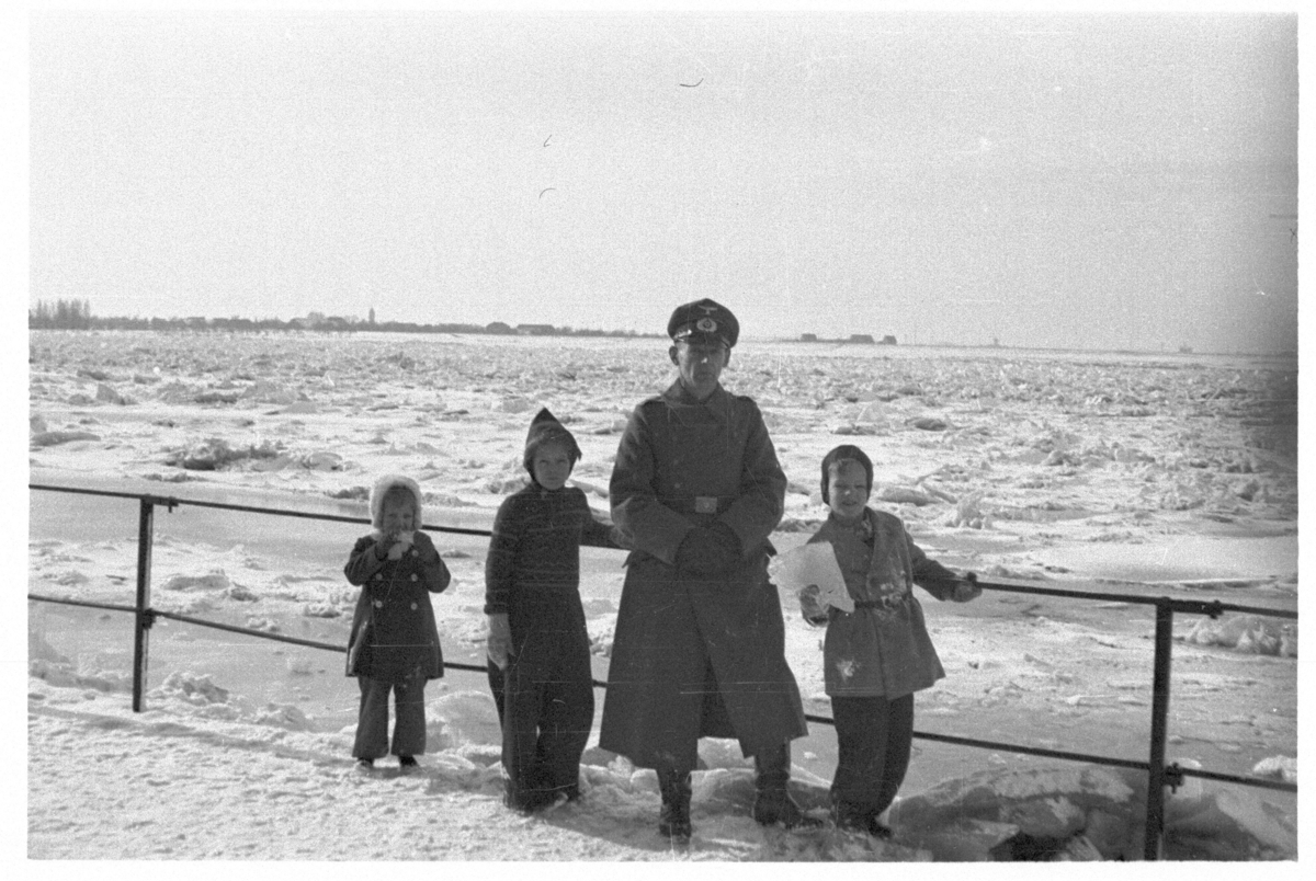 Tysk offiser, fotografert sammen med tre barn foran en islagt innsjø eller elv.