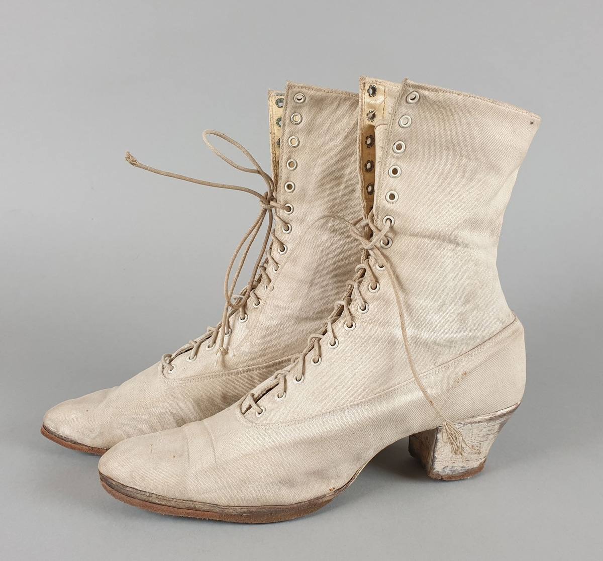Hvite damestøvletter av lerret, med snøring foran og moderat høye hæler.