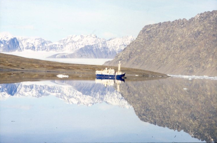 Expeditionsfartyget M/S Origo ligger för ankar i Signehamna och speglar sig i ett mycket stilla vatten.