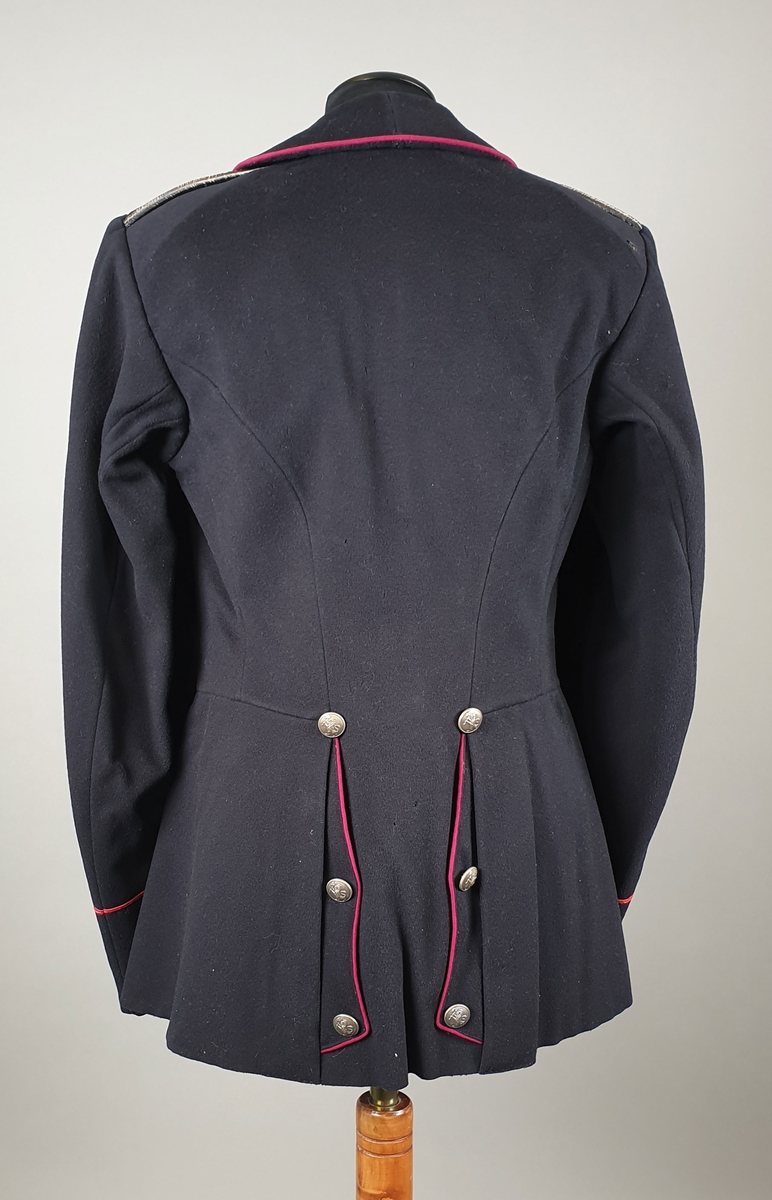 Svart uniformsjakke med mørkerøde kantbånd på krage og på ermene. Enkeltspent med metallknapper med riksvåpen. Splitt på ryggen med knapper og røde kantbånd.