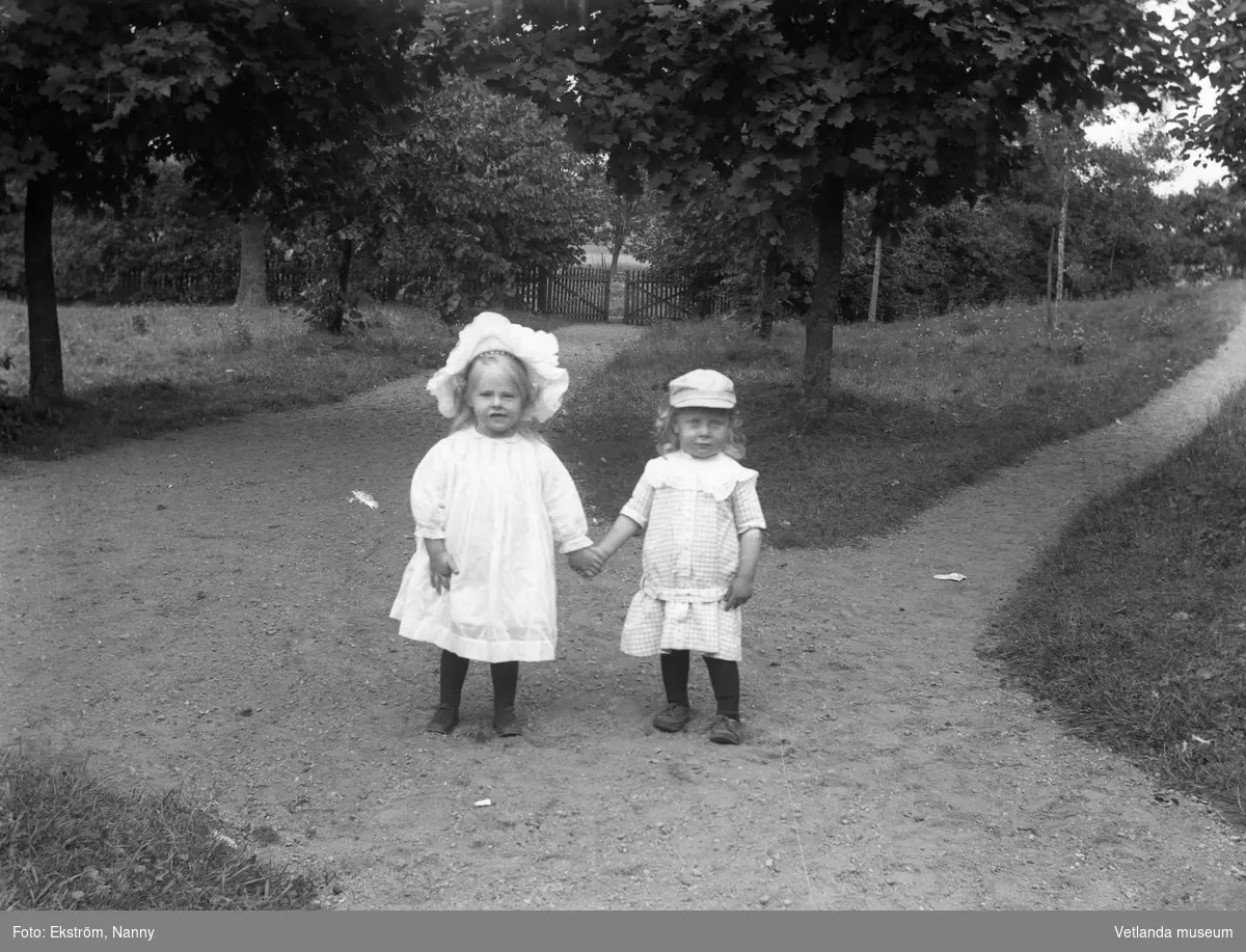 Två små barn i en trädgård eller park. Barnens anhöriga var troligtvis bekanta med fotografen.