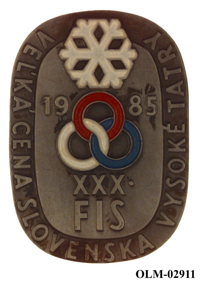 Oval minnemedalje med snøkrystall øverst, årstall under, tre ringer i rødt, hvitt og blått. Tekst rundt kanten. Medaljen ligger i et blått etui.