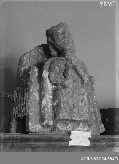 Stenskulptur av täljsten från Svarteborgs kyrka. Den helige Olof sittande i tronstol med högt ryggstöd. Han bär livbälte och mantel, en murkrona på huvudet, möjligen ett relikvarium i höger hand och håller vänster hand om skägget. Skulpturen är starkt eroderad.

Ur handskrivna katalogen 1957-1958: Olav d. helige, täljsten, Svarteborg. M: H. 41, största Br. 32,5 cm; krona och mantel, i höger hand spiran, vänster griper om skägget; sittande på en tronstol m. armstöd och högt ryggstöd, på alla håll smalnar stolen av uppåt. Starkt sliten.

Ur Katalog 1. Uddevalla Museihistoriska samlingar, svenska avdelningen. A. Yngre föremål. Upprättad av Knut Adrian Andersson 1916:                                                                                                                              No 34. Bild i täljsten av Olov den Helige. Yngre medeltiden, räknad till 1550. Förvarats i Svarteborgs kyrka under namnet "Kung Rane". Skänkt av församlingen år 1860-70-tal till Uddevalla museum. Förvaras ovanpå Medeltidsskåpet i sydvästra rummet.

Presenterad i  Uddevalla Museums tryckta katalog 1869 under rubriken 
F] Saker från yngre Medeltiden, räknad till 1550.
N:o 1. Bilder af S:t Olof i sten från Svarteborgs kyrka.

1861-1870 1 Arkeologiska och Etnografiska samlingarna U-a Museum D4A 1
Ur Gåvobok1864:
Svarteborgs församling:
Kristusbild af träd samt fragmenter af en Granit- [överstruket] Täljstensbild, enligt sägen föreställande Kung Rane, hvilka begge setat [överstruket] [oläsligt tillägg] i Svarteborgs kyrka. 
Tillagd kommentar av inrendent Knut Adrian Andersson; Olof d. Helige troligen.

Se foton på föremålet i Uddevalla museums kyrkliga utställning 1920, UMFA54467:0089.
Tillstånd, se Vårdblankett.