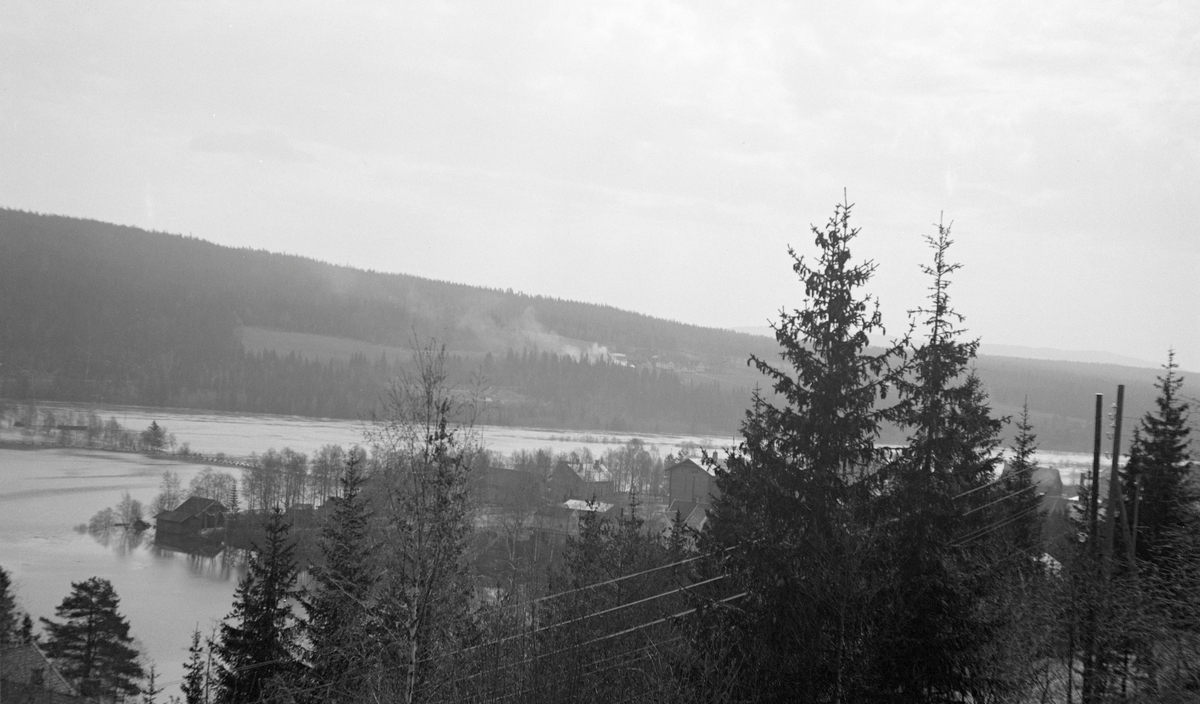 Flom i Glomma ved Rena i Åmot i Hedmark 6. mai 1934. Fotografiet er tatt fra lia på østsida av vassdraget med kameraet vendt mot den oversvømte dalbotnen, der vi kan skimte det som i dag heter Brugata med stabbesteiner som stakk opp over vannspeilet til venstre i bildet. Ellers var elvesletta oversvømt, og en del av uthusbygningene i utkanten av kommunesenteret la farlig nær vannlinja. På motsatt side av elva ser vi Ilsås-gardene i ei ellers skogkledd li.
