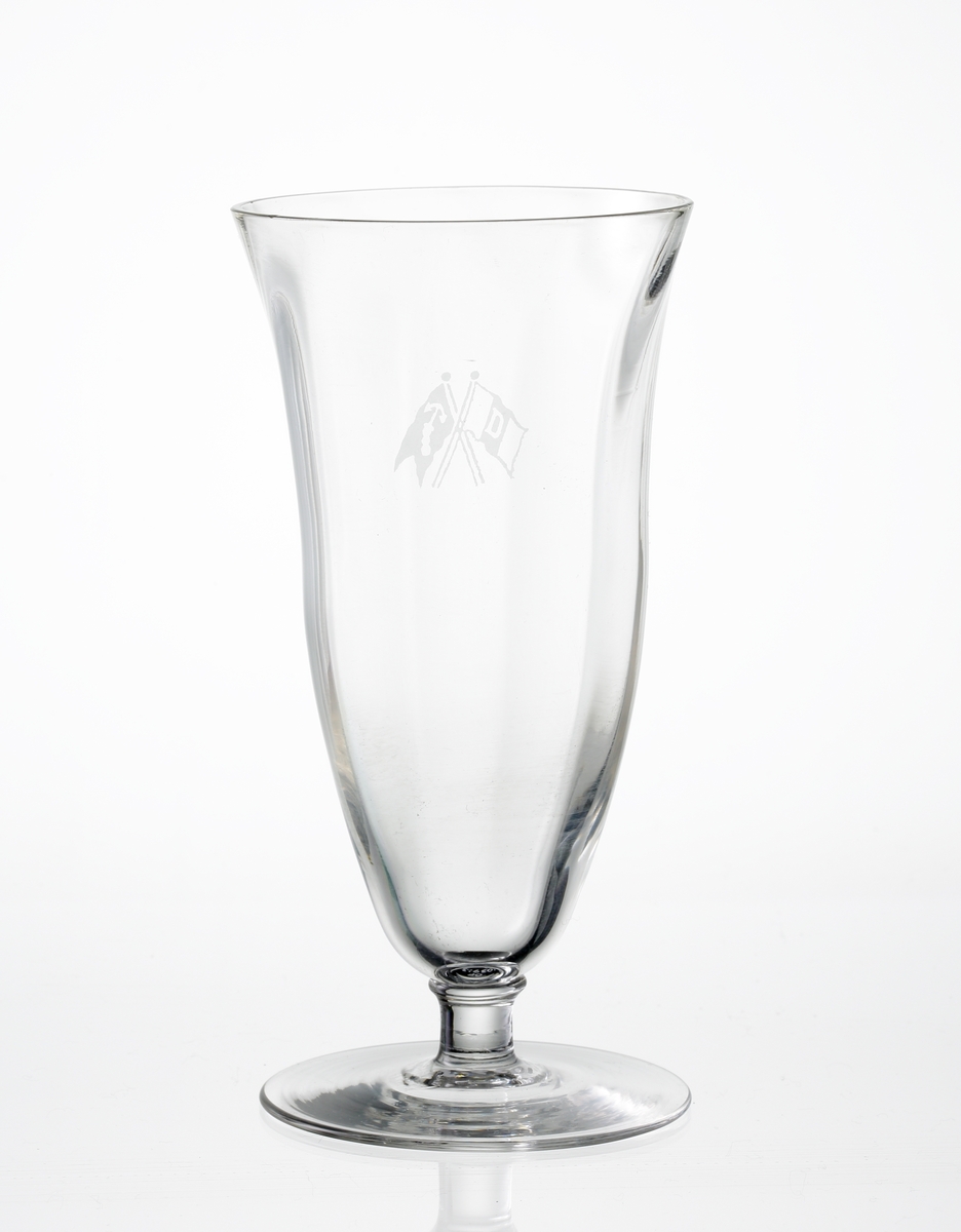 Design: Okänd. 
Champagneglas på fot. Optikblåst kupa med etsat emblem (två korslagda flaggor).