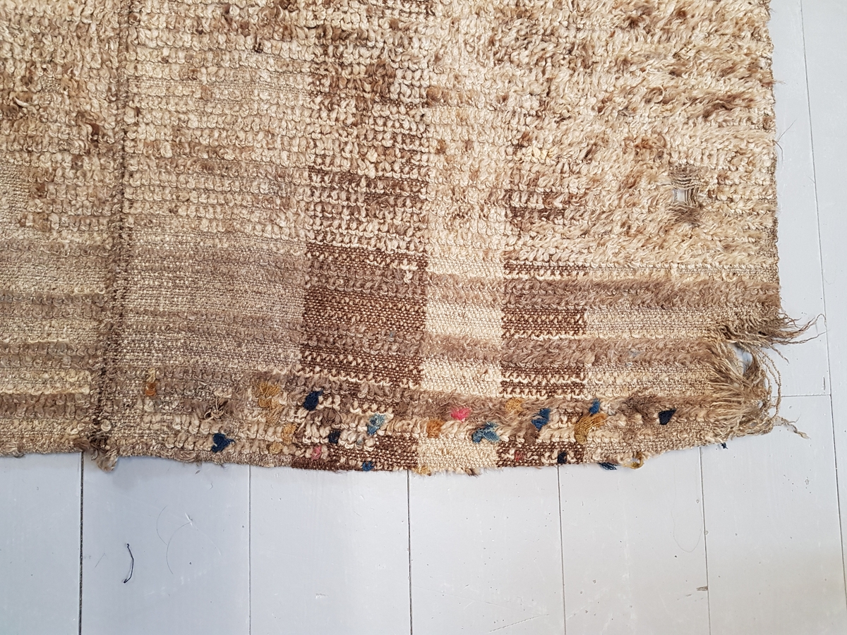 En vevd tekstil bestående av 3 lengder sydd sammen, hver lengde er på 60 cm, det er innslag av floss på tekstilen, det er ull i renning og ull i innslag vevd i diagonalkypert