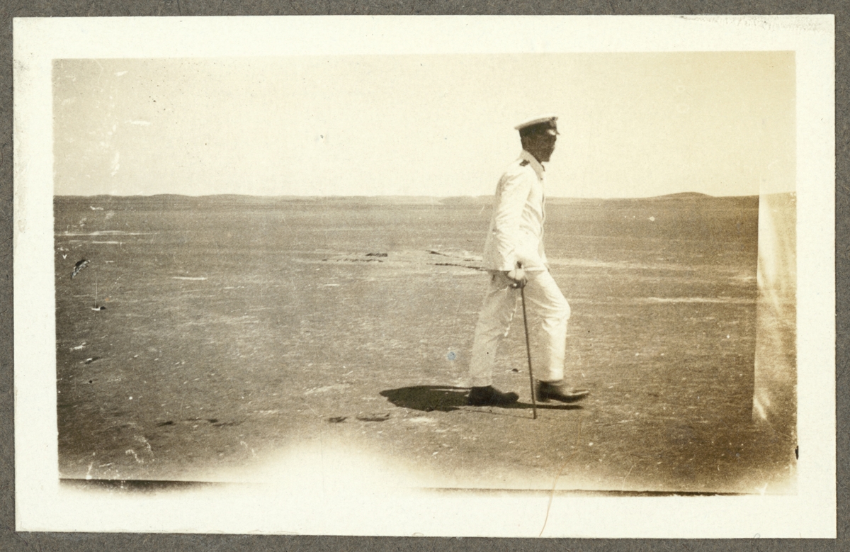 Bilden visar en befäl från Fylgia som promenerar på en strand med en käpp i handen.
