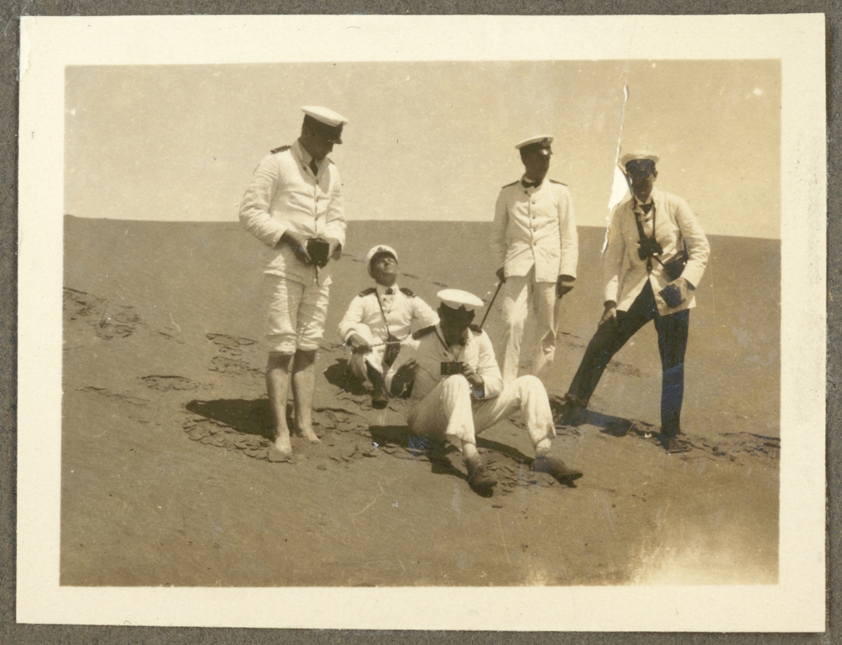 Bilden visar några sjömän från Fylgia i vit paraduniform på en sandstrand. En av de är barfotat och håller på att fotograferas. Även två av de andra har fotokameror med sig.