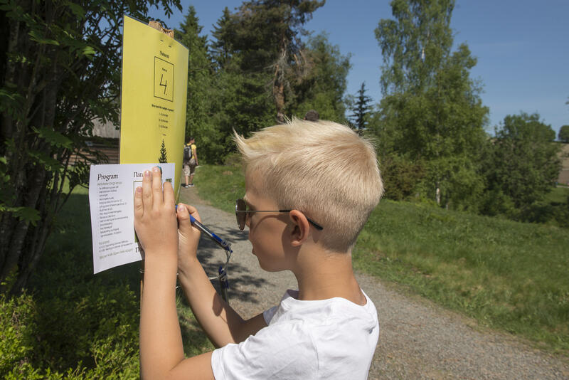 Ung gutt står og skriver på et spørsmålsark for natursti på Eiktunet friluftsmuseum.