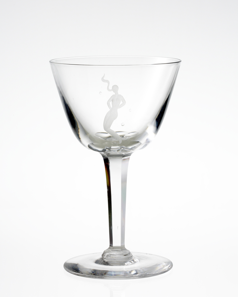 Design: Nils Landberg.
Vitvinsglas. Tulpanformad kupa med graverad sjöjungfru. Fasettslipat högt ben med bats vid fot.