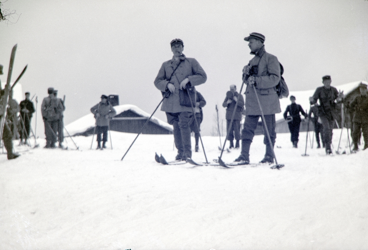 Militærøvelse i Romedal 1937. Vinterøvelse. Kronprins Olav på ski ute på tunet ved Haukåsen. Han var tilstede under øvelsen. Vinter, snø, ski, militæret.