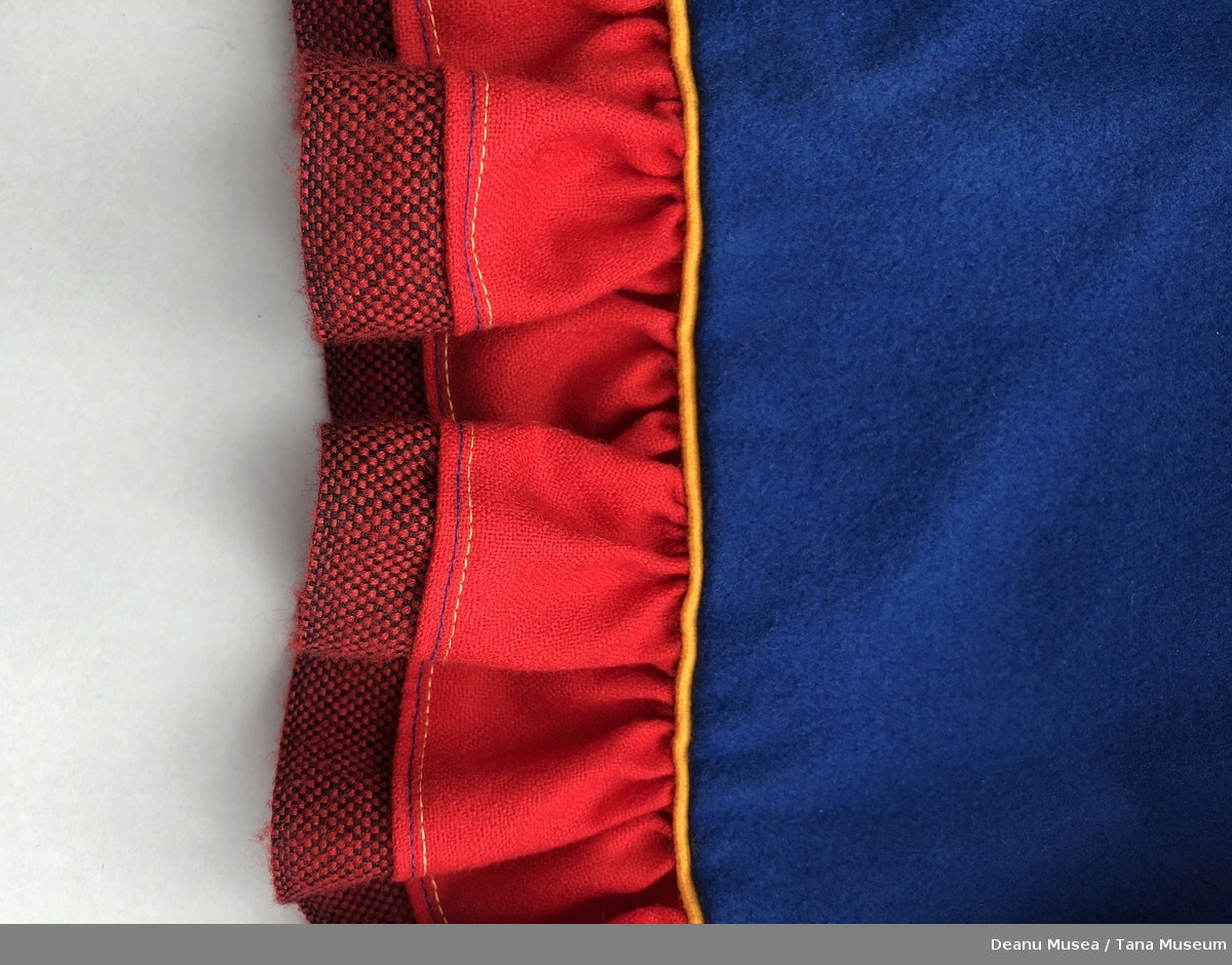 Blå kvinnekofte i ullklede fra Alleknjarg med røde pyntekanter. Rød holbi med gul og rød/svart vevet pyntekant.