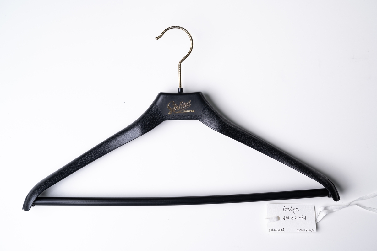 Klädgalge (kostymgalge) av svart plast med tryckt text i guld: "Ströms JÖNKÖPING". Krok av guldfärgad metall.