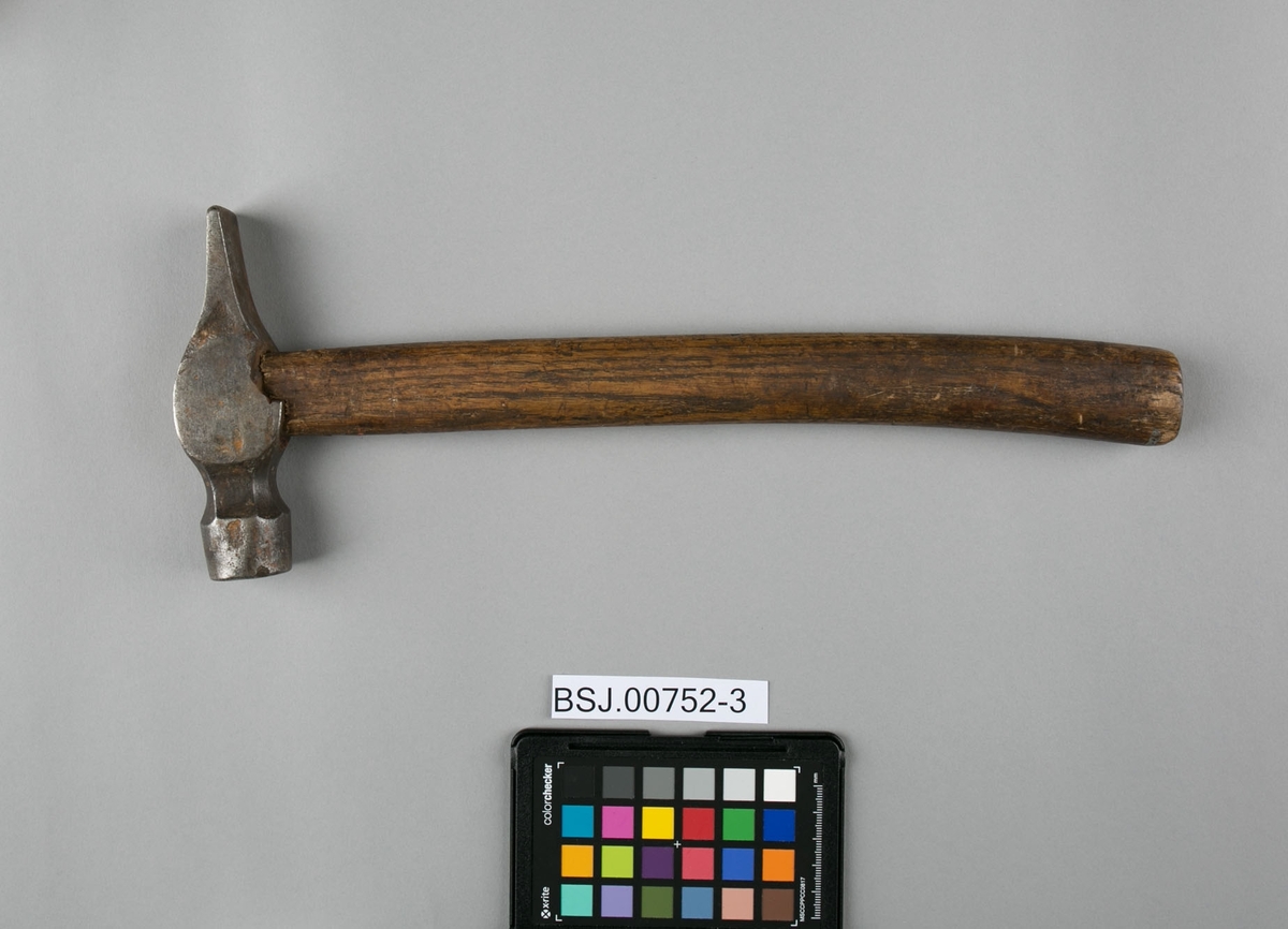 Hammer i jern med skaft av tre. Hammeren er kileformet i ene enden og butt i andre ende. 