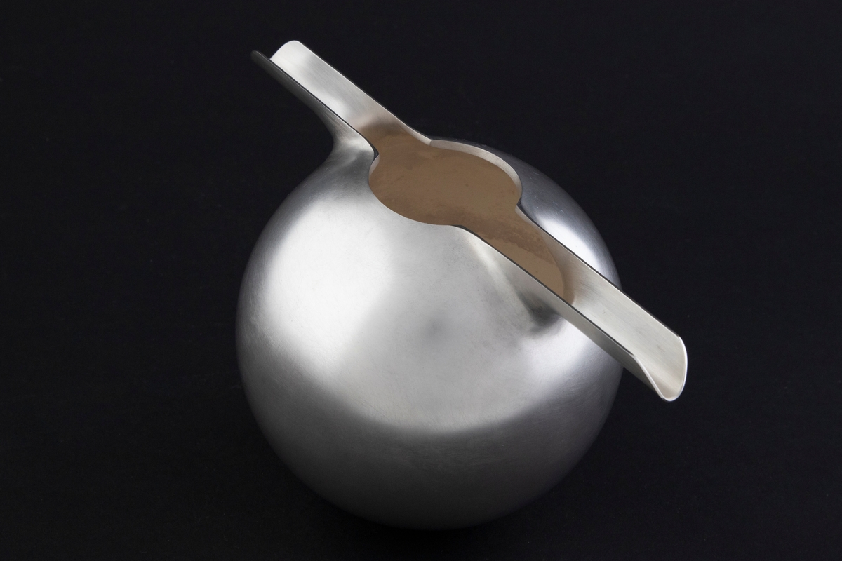Tekanne for kald te i sølv, preget av et stramt geometrisk formspråk. Kuleformet korpus med to hanker, som også fungerer som tut, på hver side av den sirkulære munningen. Overflaten er mattet.