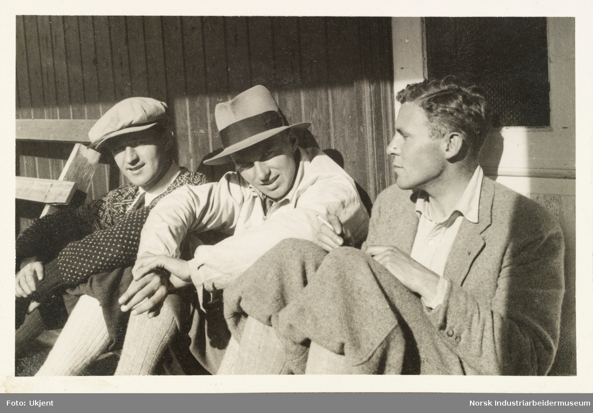 Sollitur, bededagene 1931. Tre menn med nikksers og strømper sitter utendørs foran hyttevegg. En mann med lusekoft og sikspens. En mann med hatt. Den siste mannen har ikke hodeplagg