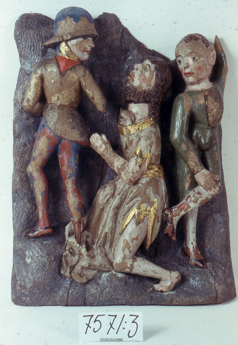 Skulptur av ek med delvis bevarad polykromi. Föreställer Johannes fängslande. I mitten Johannes i profil med knäppta händer och huvudet uppåtvänt mot en soldat. Knäböjer vänster ben, det högra dolt av den veckrika klädnaden. Soldaten i hjälm, kort rock och blåröda hosor, står med ryggen utåt och vänder huvudet mot Johannes. Griper tag i Johannes halslinning med höger hand. Till höger om Johannes en korthårig ung man i grön åtsittande dräkt, röda strumpor och svarta skor. Står frontalt med höger hand på det böjda vänstra benet. Vänster arm uppåtsträckt, handen borta. Vänder huvudet snett mot Johannes. Delar av alla klädedräkterna förgyllda. Soldatens högra fot borta, liksom 30 m.m. av hans högra underarm. Ansiktsfärgen på samtliga figurer skadad. Delvis urholkad på baksidan. Troligen svenkt arbete.  Del av ett altarskåp. Se Bengt Söderberg: "Skara Stift i ord och bild" sidan 670 
"Herman Fridholm" Edsvära hembygdsbok sidorna 66 och 67.