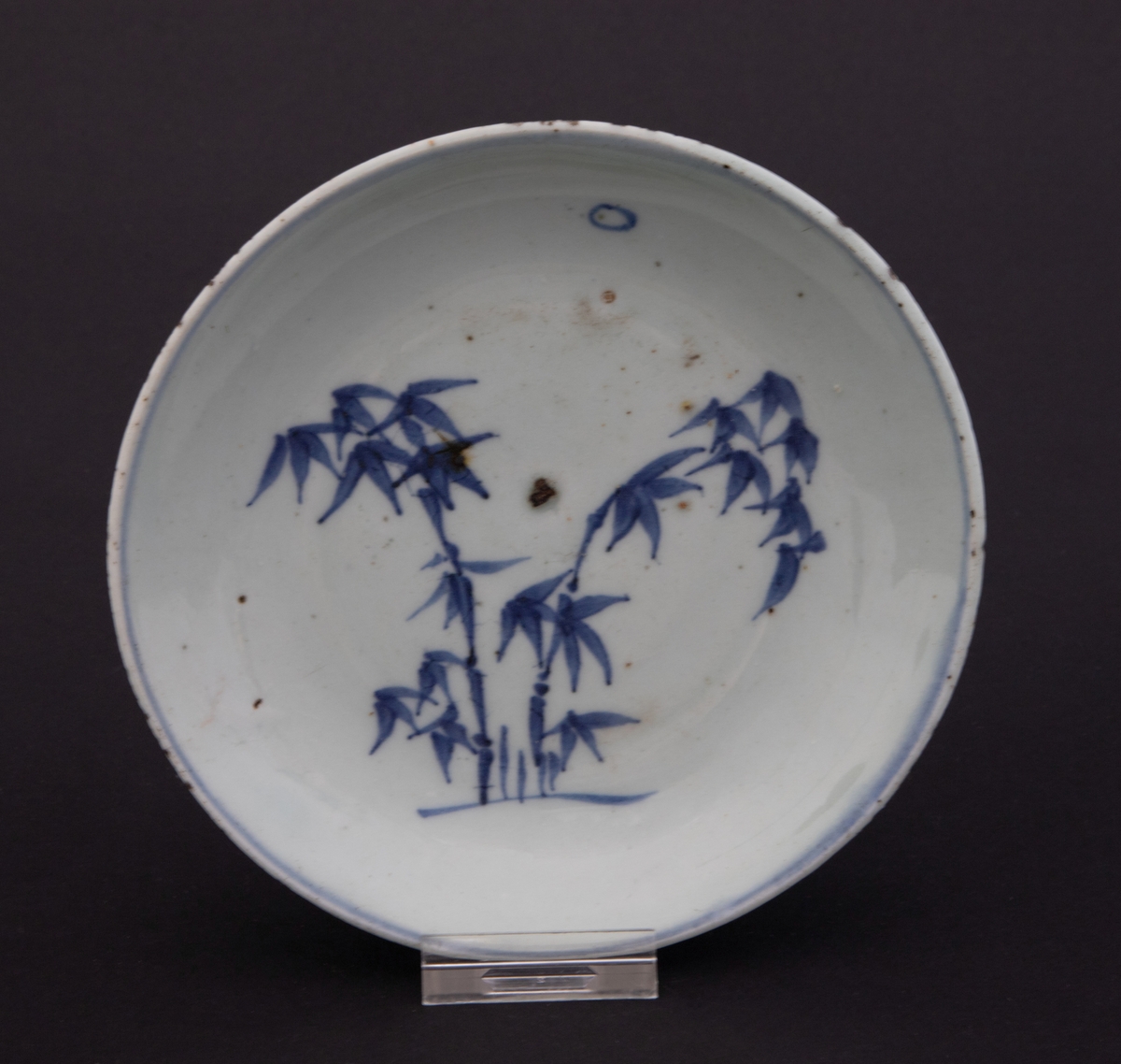 Motiv i koboltblå underglasur som forestiller bambus i måneksinn. Koboltblå ring rundt kanten.