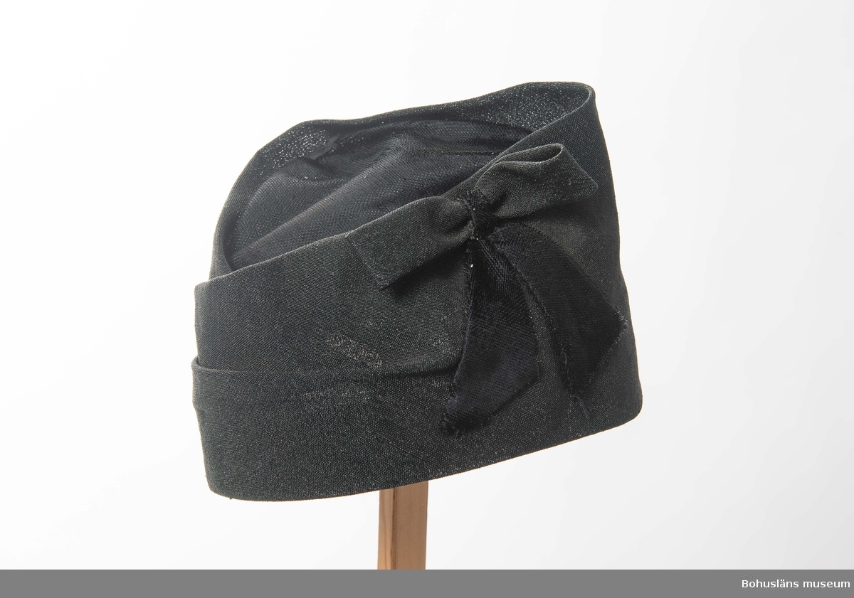 471 Tillverkningstid 1950-TAL
394 Landskap BOHUSLÄN

Svart hatt med draperingar och rosett. Glansigt tyg upptill och på rosettbanden. 
Fodrad med taft.