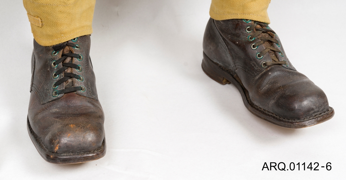 Korte Feltstøvler i skinn med snøring, sålen er festet med små nagler som er synlig under foten. Sålen er delvis gummi.