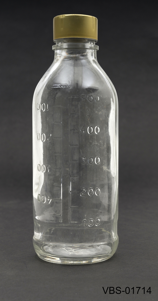 Glassflaske som måleglass (100 til 500 ml) med to lokk i metall og en gummi propp.
Sylindrisk måleglass som smalner i øvre del. 
Lokket er gylt og virker ved trykk. Den indreskrulokk er laget av aluminium og den sentrale delen er perforert. En tredje gummipropp forsegler innholdet i flasken.
Målingene på flasken er trykt for å brukes i begge retninger.