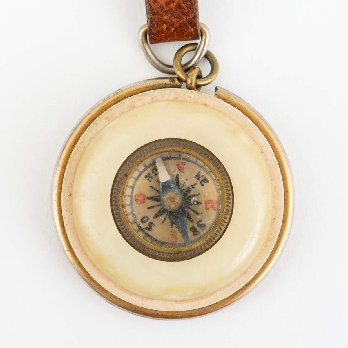 Et rundt kompass i lommeformat med reim. Selve kompasset er satt inn i skiver av antatt bakelitt. Reima er laget av lær. Beslag av messing.
