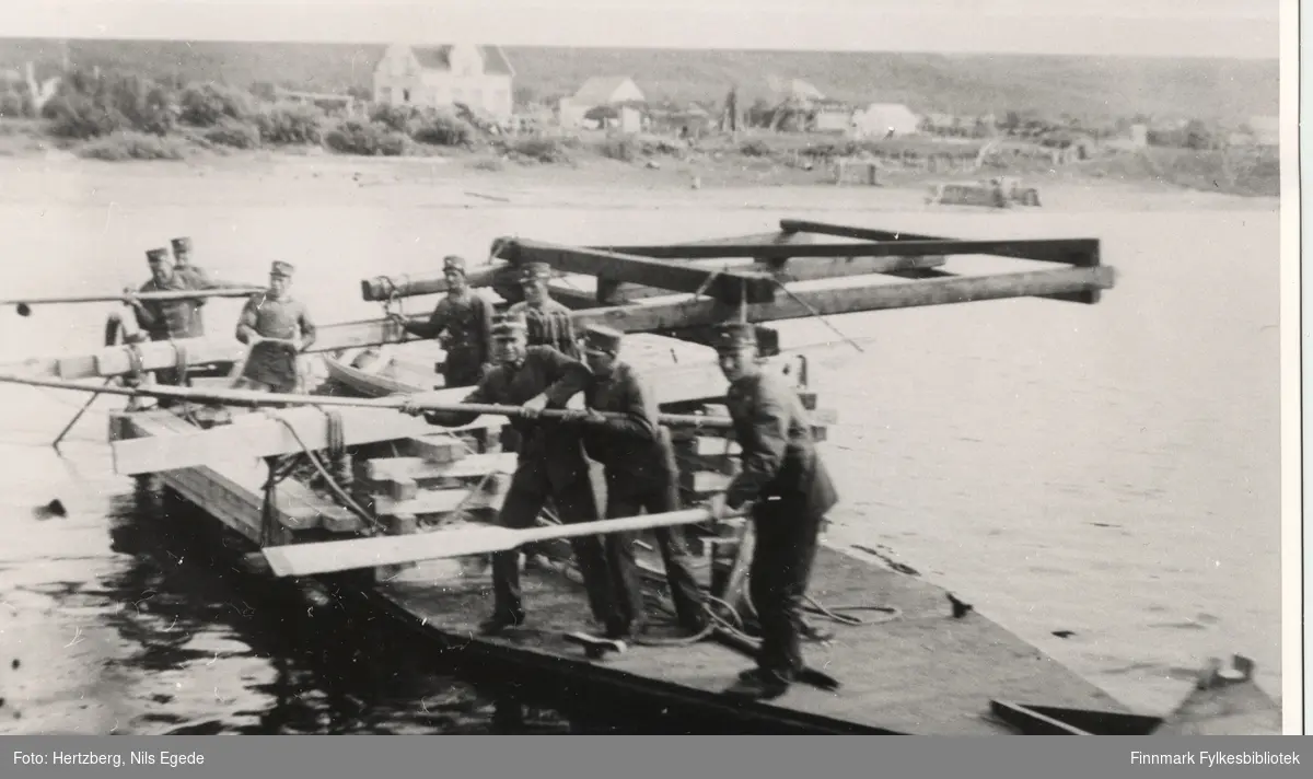 Åtte menn holder på med brubygging i Seida. De er på en flåte midt på Tanaelven hvor de haler bukkene inntil. Seida-Tana, 1939.
