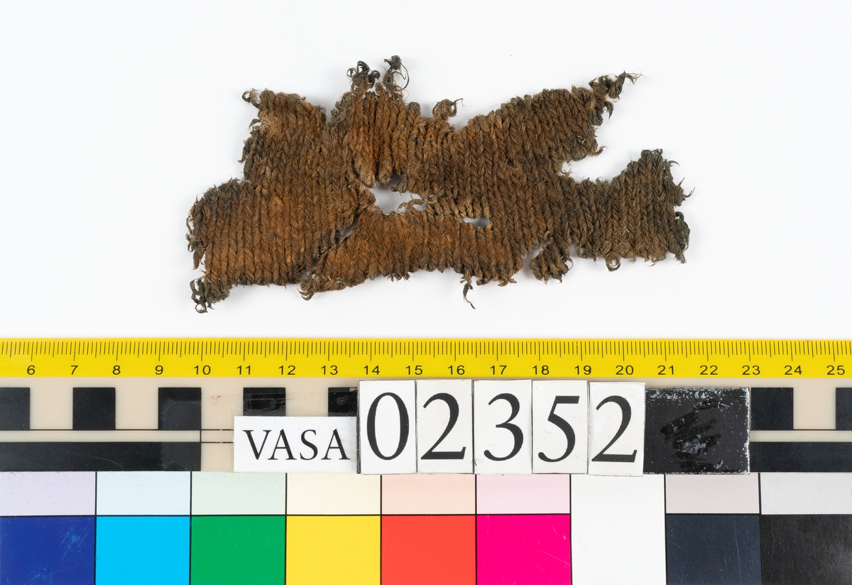 Ett textilfynd som hittades längst ned i hålskeppet på styrbord sida vid balk 20-21. Fyndet är ett så kallat lösfynd då det inte hittades vare sig i samband med mänskliga kvarlevor eller i ett slutet fynd så som en tunna eller kista. Fyndet består av ett mindre slätstickat fragment av ull med en ökning och en minskning. Fragmentet har troligen varit en del av en dräkt men har ingen ytterligare information som kan berätta vad det ursprungligen kan ha varit. Textilen är ett av de få stickade fynden från Vasa.

För mer detaljerad information från textildokumentationen (år 2021) se länkade filer.